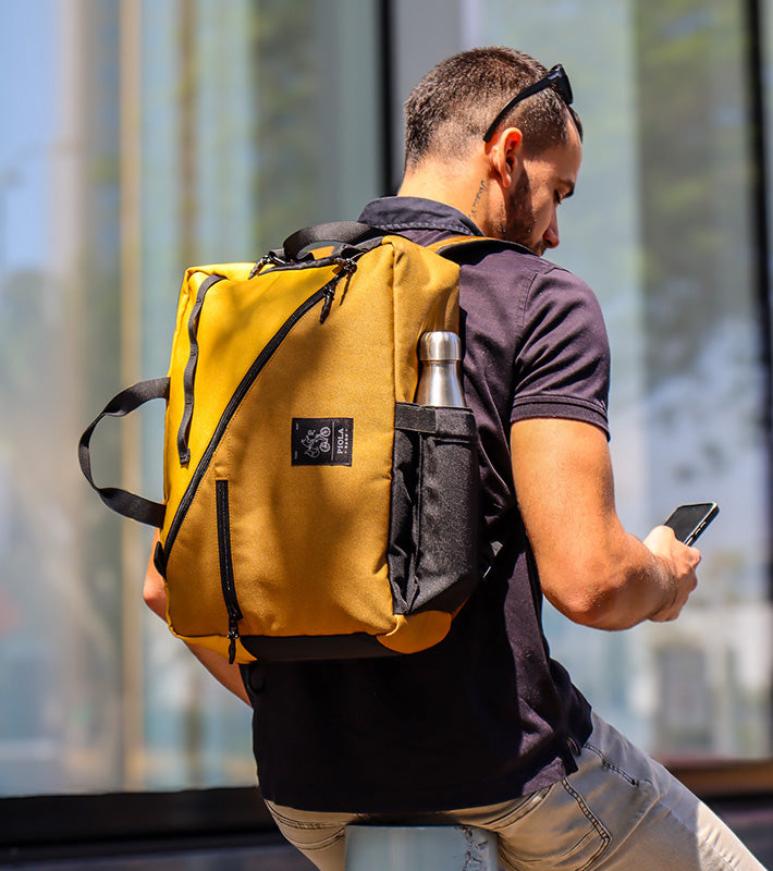 Mochila mostaza Piola Bags en la espalda de un joven mientras revisa su celular